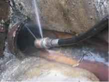 Jetting nozzle spraying into a pipe opening